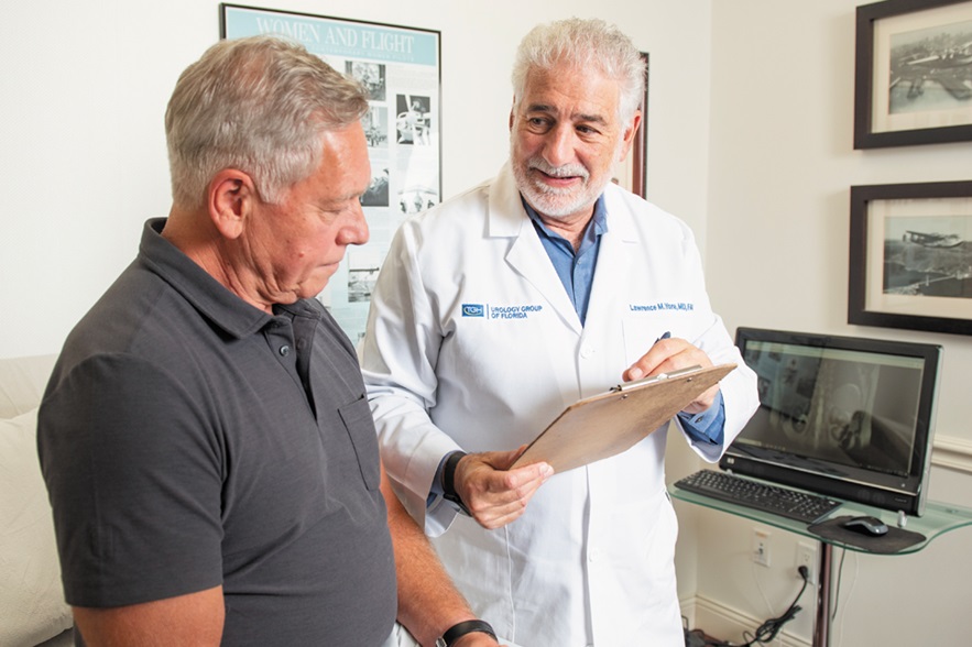 a tgh urology group of fl physician speaks with his middle-aged male patient about prostate cancer while holding a clipboard and pen