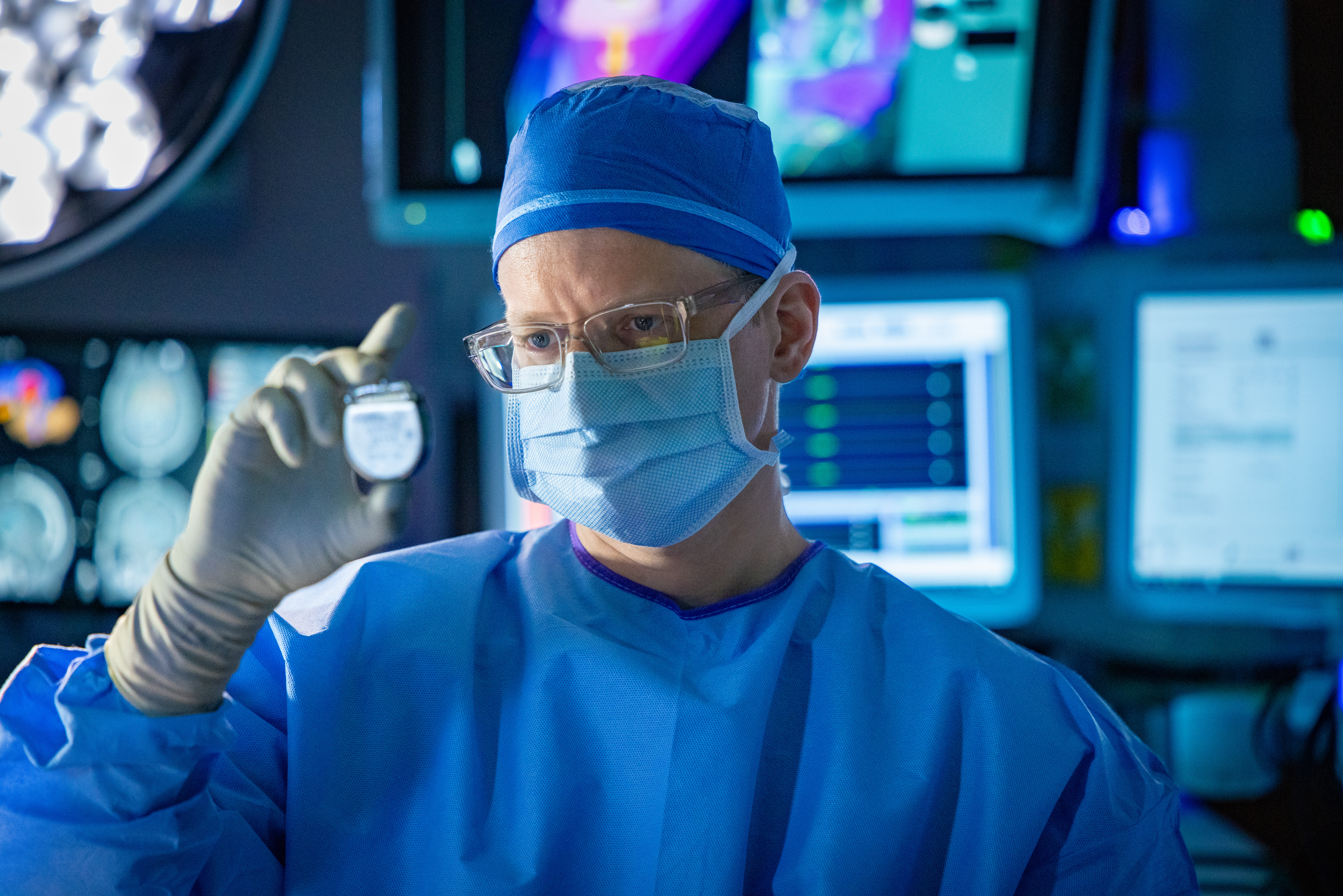 Surgery scene with the O-Arm and Dr. Yarema Bezchlibnyk of the TGH Neuroscience Institute in an operating room with lights and monitors in background